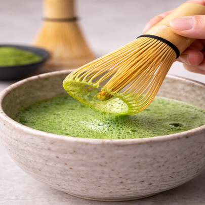 Close-up of bamboo matcha whisk lifting creamy green matcha foam showing fine froth texture